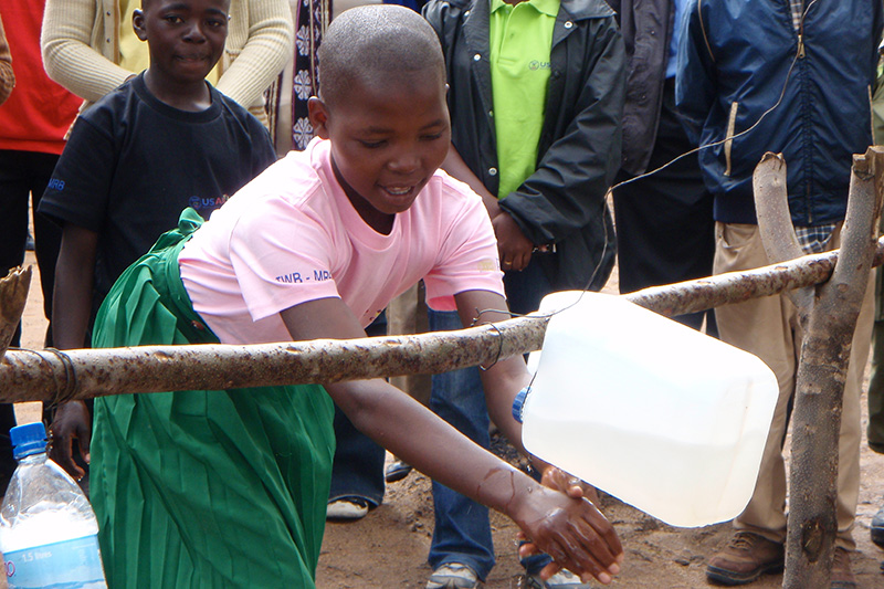 child washing hands with bucket of water